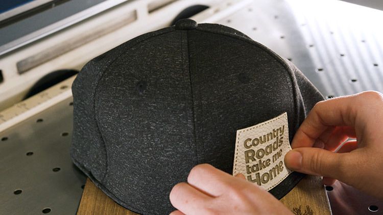 Hands aligning a laser engraved leather patch on a dark baseball cap