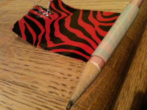 A hand uses duct tape wrapped around a pencil as a grip.