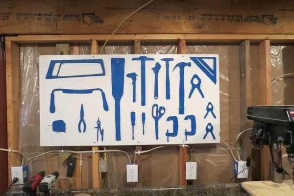 Silhouettes of varying tools painted onto a peg board and hung in a garage setting.